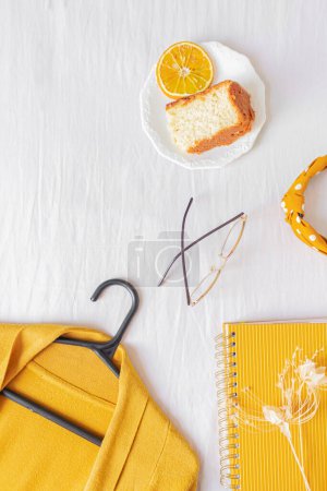 Téléchargez les photos : Bureau à domicile cadre avec ordinateur portable, morceau de gâteau orange, cardigan, lunettes et planificateur sur fond blanc. - en image libre de droit