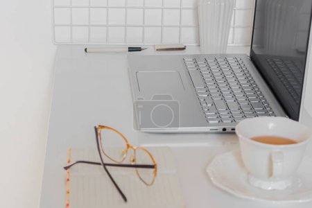 Téléchargez les photos : Concept d'entreprise. Bureau à domicile minimaliste avec ordinateur portable, tasse de thé et fournitures fixes - en image libre de droit