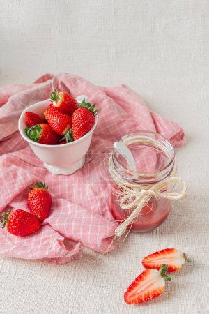 Photo for Strawberry marmalade on a jar, a tiny white spoon inside and fresh strawberries on a bowl. Light background. Seasonal eating concept. - Royalty Free Image