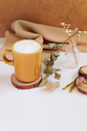 Photo for Latte, cinnamon, wooden coaster and dry leaves and flowers on beige background. Fall, autumn concept. - Royalty Free Image