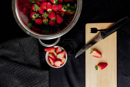 Photo for Strawberries in a bowl, some strawberries cut on the cutting board, on a black background. - Royalty Free Image