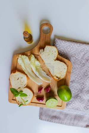 Foto de Cocina Mediterránea - Tabla de cortar preparada para hacer una buena ensalada seguida de pan como plato de inicio. Aceite de oliva, acelga, albahaca, ajo, limón y un trozo de pan fresco. - Imagen libre de derechos