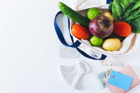 Téléchargez les photos : Carte de crédit et sac écologique avec des légumes sur fond blanc. Pose plate, vue du dessus, espace de copie. - en image libre de droit