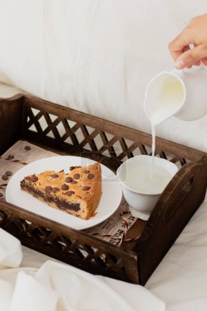 Photo for Female hand pouring milk into the cup near the slice of cookie pie on wooden tray - Royalty Free Image