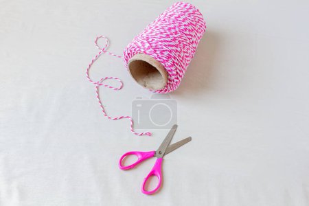 Téléchargez les photos : String rayé rose et ciseaux sur fond blanc. Concept artisanal. - en image libre de droit