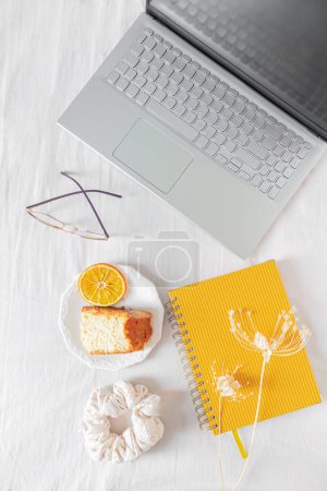 Photo for Home office desk frame with laptop, orange piece of cake, planner, glasses, scrunchie and dried flowers on white background. - Royalty Free Image