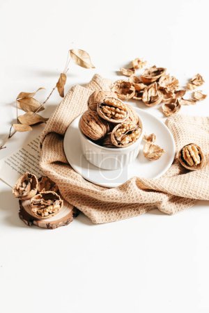 Photo for Cosy autumn composition of walnuts in white plate and craft paper on white background. - Royalty Free Image