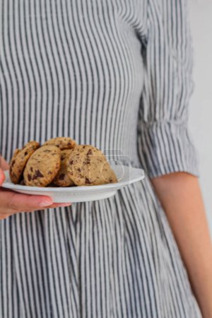 Téléchargez les photos : Femme portant une robe à motifs rayés et tenant une assiette pleine de biscuits - en image libre de droit