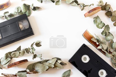 Photo for Video cassette, old-fashioned camera films, dried branches of eucalyptus leaves, and wood pieces on white background. Flat lay, overhead view, top view. Vintage frame composition. - Royalty Free Image