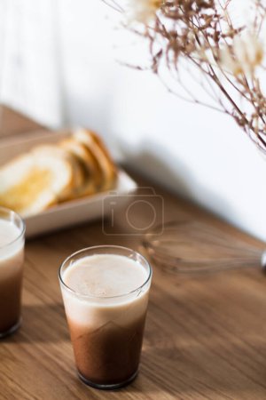 Foto de Composición otoñal con café dalgona con leche en vasos, tostadas frescas y batido sobre mesa de madera. - Imagen libre de derechos