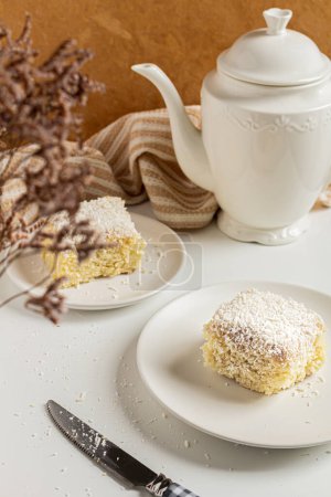 Photo for Breakfast beige cozy composition with coconut cake in plates and white teapot - Royalty Free Image