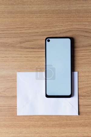 Photo for Top view of smartphone with white screen lying on white envelope on wooden background - Royalty Free Image