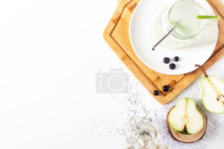 Photo for Aesthetic minimalist composition. Glass with green lemonade, pear halves and blueberries on white background. Summer cold drink concept. - Royalty Free Image