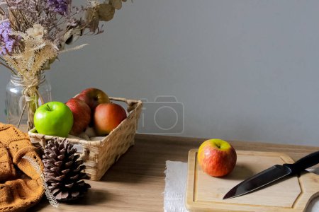 Foto de Composición otoñal con canasta completa de manzanas y manzana entera con cuchillo sobre tabla de madera - Imagen libre de derechos