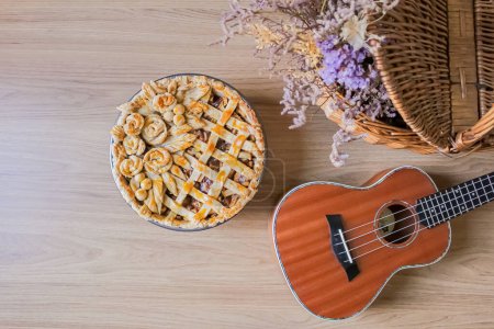 Téléchargez les photos : Tarte aux pommes maison sur une table avec des fleurs séchées et ukulélé. Composition d'automne - en image libre de droit