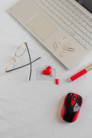 Foto de Espacio de trabajo de escritorio de oficina en casa con computadora portátil, gafas, lápiz labial rojo, clips de papel y divisor de audio del corazón sobre fondo blanco. - Imagen libre de derechos