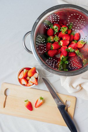 Photo for Top view of strawberries in a metal colander and some strawberries cut on the cutting board - Royalty Free Image