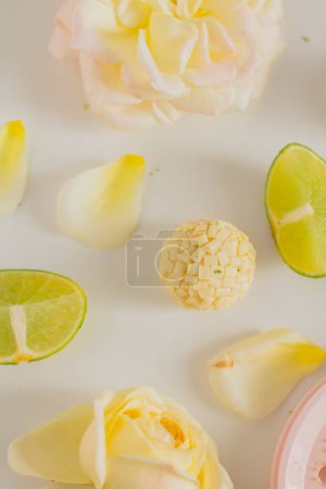 Téléchargez les photos : Bonbons au chocolat blanc avec tranches de citron et fleurs roses sur fond blanc. Style alimentaire. Réconfort du printemps et de l'été. - en image libre de droit