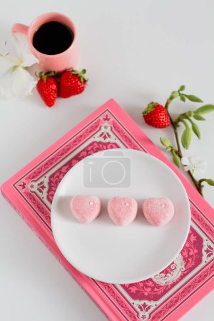 Téléchargez les photos : Composition alimentaire de printemps confort. Bonbons roses sur plaque blanche avec fraises fraîches et tasse de café de côté - en image libre de droit