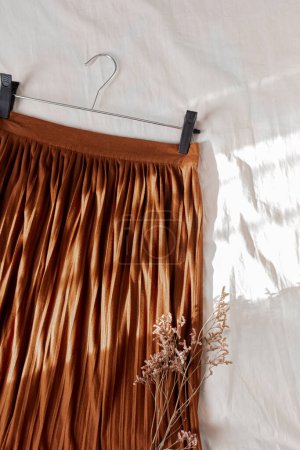 Téléchargez les photos : Composition des femmes de mode avec belle jupe plissée marron élégant sur couverture en lin blanc. Couché à plat, vue de dessus. Concept de mode. - en image libre de droit