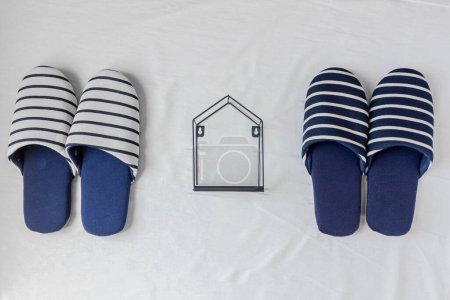 Foto de Dos pares de zapatillas y una casita sobre un fondo de tela blanca. Rutina diaria después del matrimonio. - Imagen libre de derechos