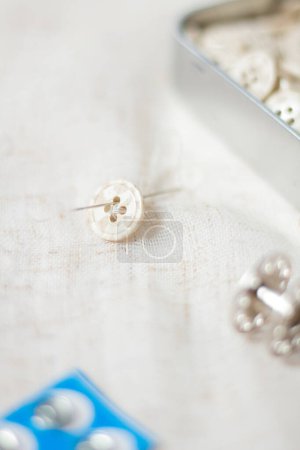 Foto de Composición de costura con botones beige en la caja y una aguja que pasa a través del botón en tela ligera - Imagen libre de derechos