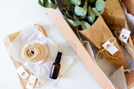 Téléchargez les photos : Bouteille marron avec fil et bouquets d'eucalyptus vert en boîte artisanale sur fond blanc. - en image libre de droit