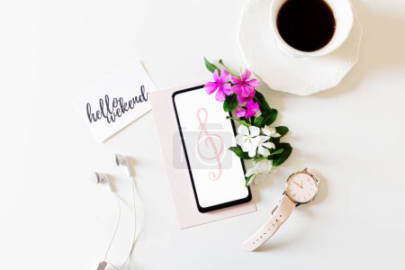 Photo for Wekeend concept. Earphones, mobile phone, wrist watch, cup pf coffee, card with the quote: "hello weekend" and pink, white flowers on white background. Flat lay, top view. - Royalty Free Image