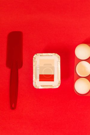 Téléchargez les photos : Emballage de livraison, spatule et œufs sur fond rouge. Composition de style alimentaire moderne. Concept de confiserie. - en image libre de droit