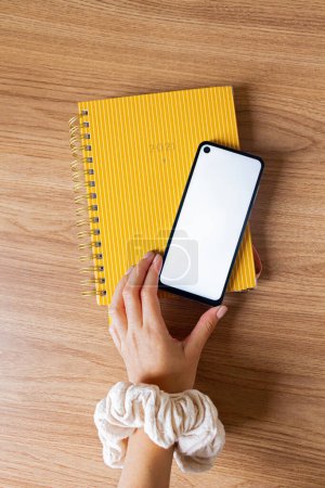 Photo for Hand holding smartphone and notebook on table top view. - Royalty Free Image