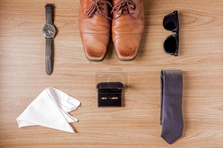 Photo for Male elegant accessories. Brown shoes on a wooden background. Top view of belt, golden wedding rings, wrist watch, tie and sunglasses. Preparation for a wedding concept. - Royalty Free Image