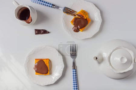 Foto de Mesa servida con rodajas de pastel de zanahoria brasileña, jarra con chocolate y tetera - Imagen libre de derechos