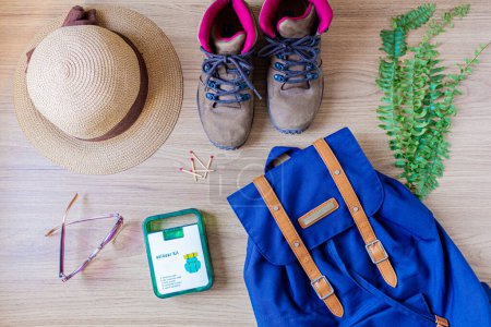 Foto de Fondo de madera con botas femeninas trekking, fósforos, gafas de sol, botiquín, hojas, sombrero de paja y mochila. - Imagen libre de derechos