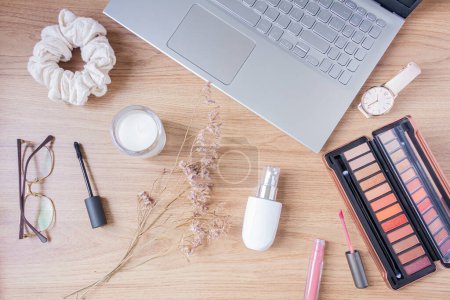 Photo for Beauty blog fashion concept. Female styled accessories: laptop, scrunchie, wildflowers and cosmetics on wooden background. Flat lay, top view trendy feminine background. - Royalty Free Image