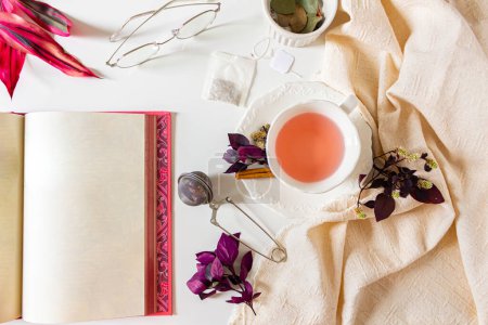 Foto de Copa de composición de té de jengibre con hojas púrpura y rosa, canela, colador de té, bolsa de té sobre fondo blanco. Asiento plano, vista superior. Concepto de hora del té. - Imagen libre de derechos