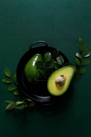 Photo for Top view of sliced raw avocado in pan decorated in green leaves all green arrangement. Flat lay, Creative food concept. - Royalty Free Image