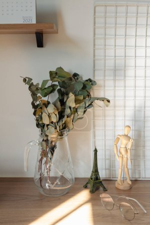 Téléchargez les photos : Branches d'eucalyptus dans un vase en verre avec des ombres de lumière du soleil sur le bureau. Design de décoration intérieure romantique. - en image libre de droit