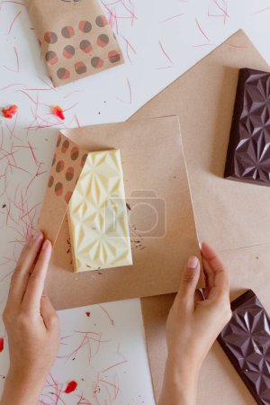 Foto de Manos femeninas envolviendo barra de chocolate en papel artesanal. Concepto de estilo de alimentos. - Imagen libre de derechos