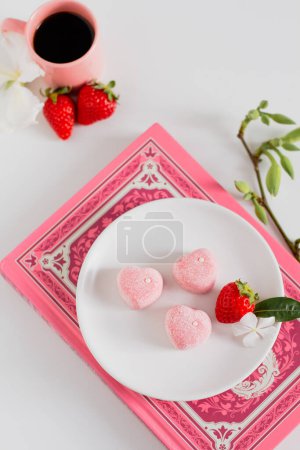 Foto de Composición de alimentos confort primavera. Dulces rosados en plato blanco con fresas frescas y taza de café aparte - Imagen libre de derechos