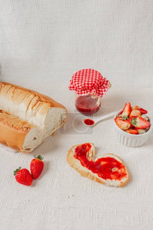 Foto de Fondo de tela de lino blanco con un frasco de mermelada de fresa, un tazón lleno de fresas frescas y un delicioso pan. - Imagen libre de derechos