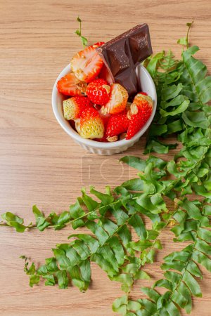 Photo for Strawberries in bowl and a piece of chocolate on a wooden background. - Royalty Free Image