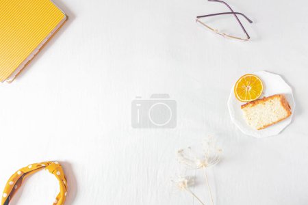 Téléchargez les photos : Composition de cadre de bureau à domicile avec morceau orange de gâteau, lunettes, bandeau et planificateur sur fond blanc. Pose plate, vue de dessus nature morte concept. - en image libre de droit