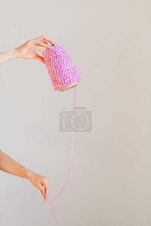Téléchargez les photos : Mains féminines tenant rouleau de ficelle rose. Concept artisanal. - en image libre de droit