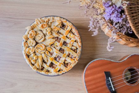 Foto de Tarta de manzana decorada sobre una mesa con flores secas y ukelele. Composición otoñal - Imagen libre de derechos