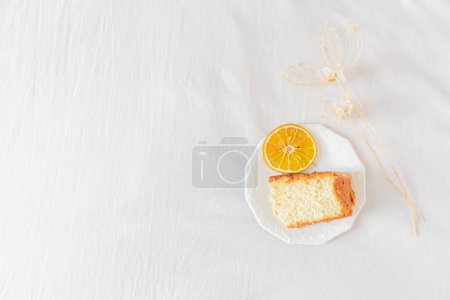 Photo for Breakfast composition with orange piece of cake on white plate on white textile background. Flat lay, top view. - Royalty Free Image