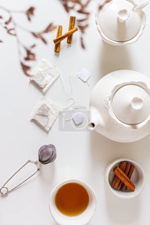Photo for Composition with cup of tea, teapot, sugar pot, tea strainer, cinnamon and tea bag on white background. Flat lay, top view. Slow morning concept. - Royalty Free Image