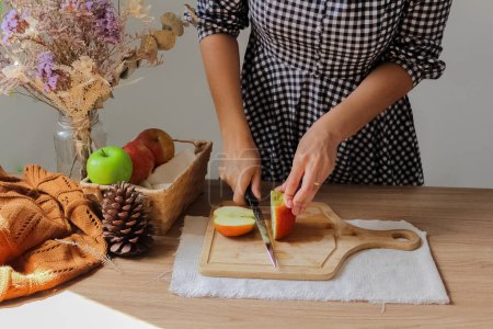 Photo for Cropped shot of woman in checkered dress cutting apples on wooden board - Royalty Free Image