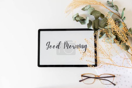 Téléchargez les photos : Vue du dessus de la tablette numérique avec phrase Bonjour à l'écran et fleurs séchées de côté sur fond blanc - en image libre de droit