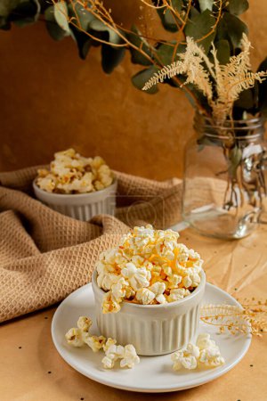 Photo for Cozy and aesthetic beige composition with popcorn decorated with dried plants and kitchenware. Autumn, winter food concept. - Royalty Free Image