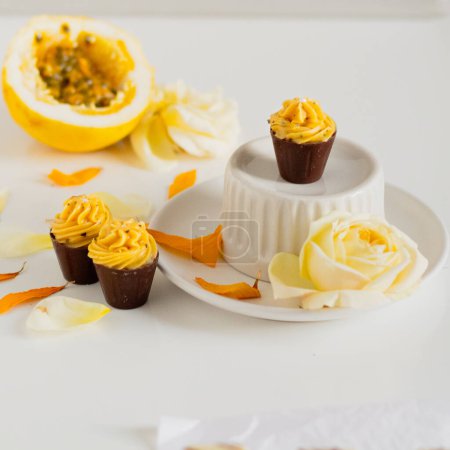 Photo for Homemade cupcakes on kitchenware with passion fruit and floral petals around - Royalty Free Image